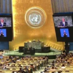 Assemblea Generale delle Nazioni Unite con intervento dal podio e simbolo ONU sullo sfondo.