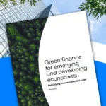 Copertina del report ICC “Green finance for emerging and developing economies: Rethinking macroprudential rules” sovrapposta a uno sfondo con edifici moderni, cielo e elementi naturali, a rappresentare il tema della finanza sostenibile.